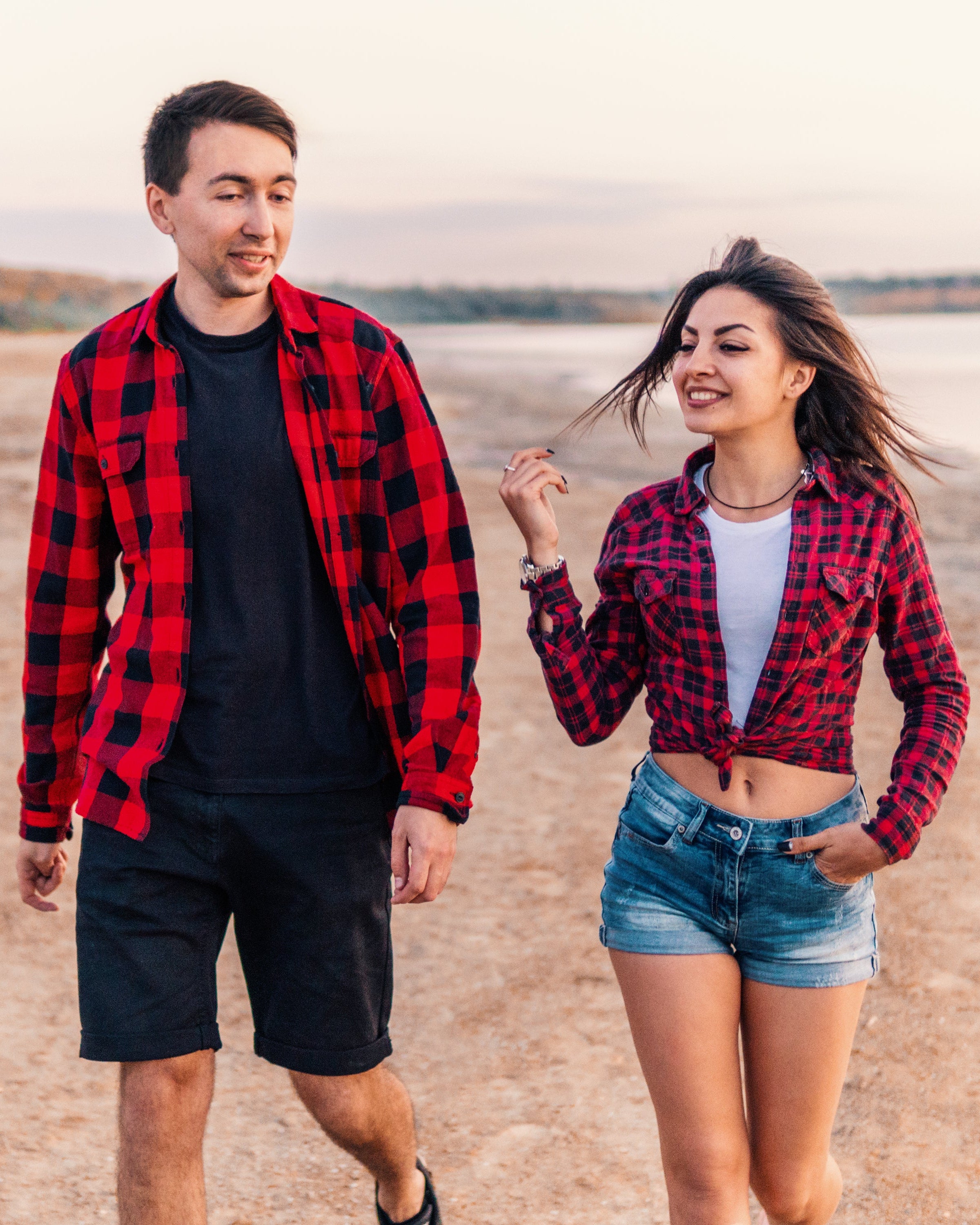 Two people wearing red and black plaid shirts walking on a beach.